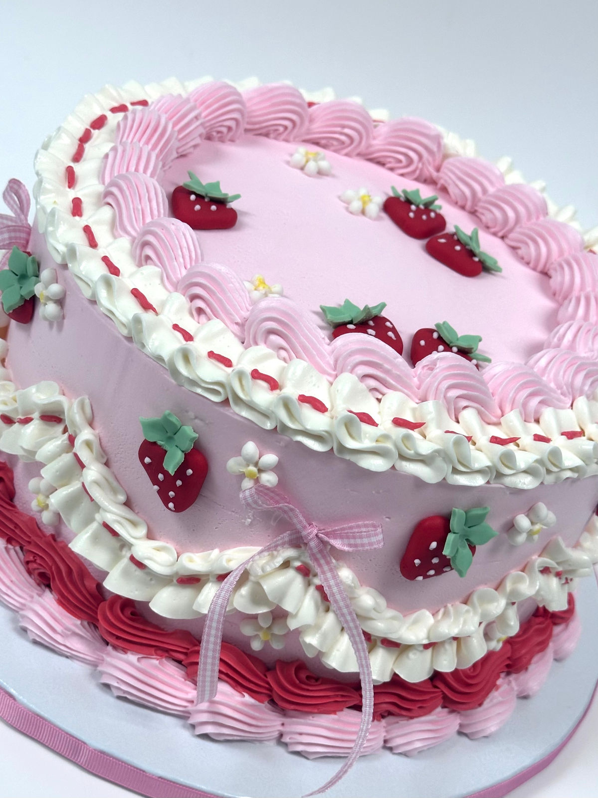 A pink vintage buttercream cake piped with shell borders and topped with sugar strawberries