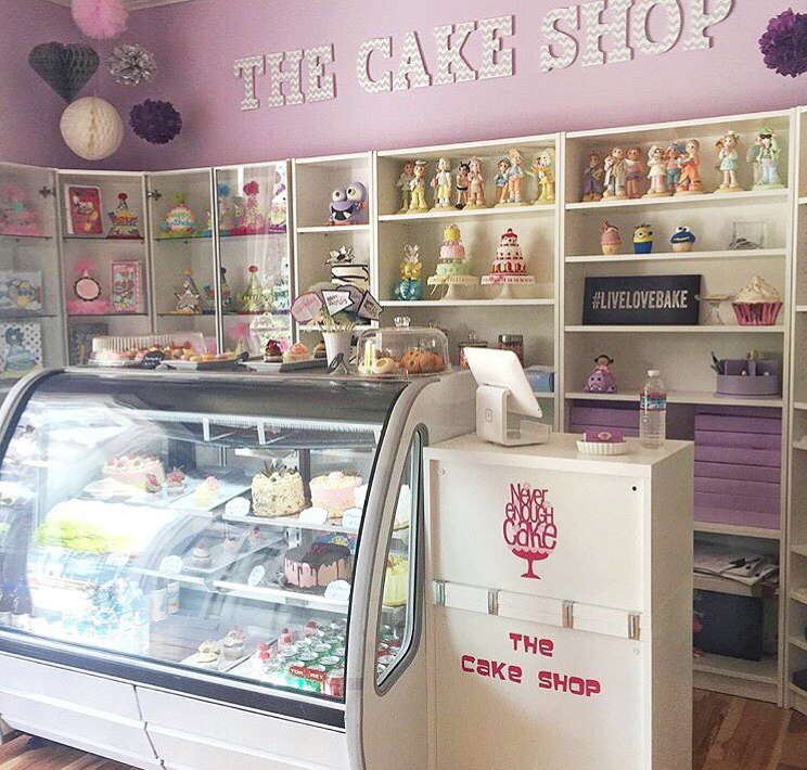 Inside The Cake Shop in San Mateo, with the display case of cakes and treats below the shop sign